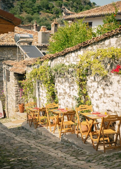 Free Sunny outdoor cafe with wooden chairs on a cobblestone street in historic Berat. Stock Photo