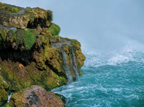 Serene waterfall cascading down a rugged cliff into turquoise waters, reflecting nature's beauty.