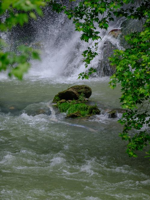 Free A picturesque waterfall cascading over moss-covered rocks amidst vibrant greenery. Stock Photo