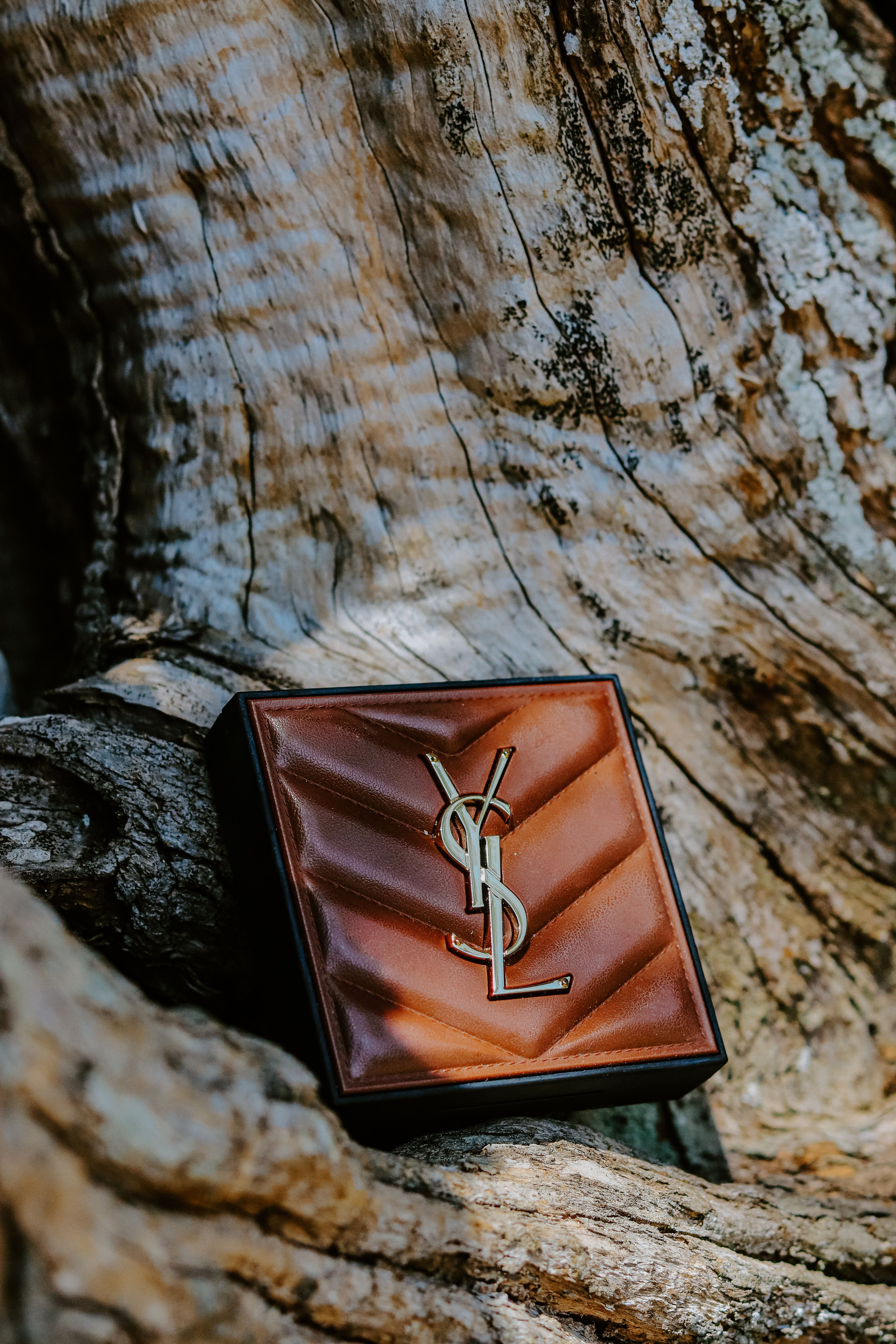 Elegant brown leather wallet with logo on a textured wooden surface outdoors.