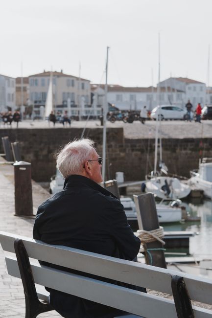 An elderly man sits peacefully overlooking a harbor in Nuova Aquitania, Francia, on a calm day.