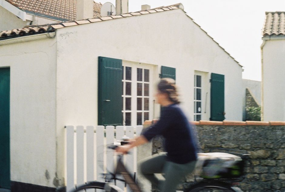 A blurred cyclist passes by a quaint cottage in Nuova Aquitania, France, showcasing rustic charm.