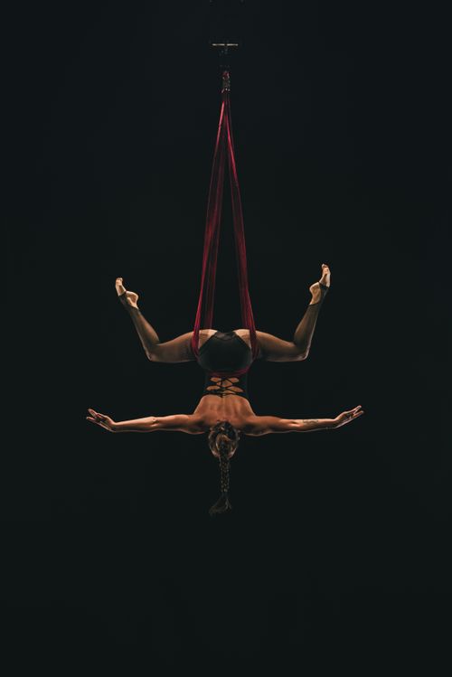 Free Aerial acrobat gracefully performs upside down art with silk ribbons in dramatic lighting. Stock Photo