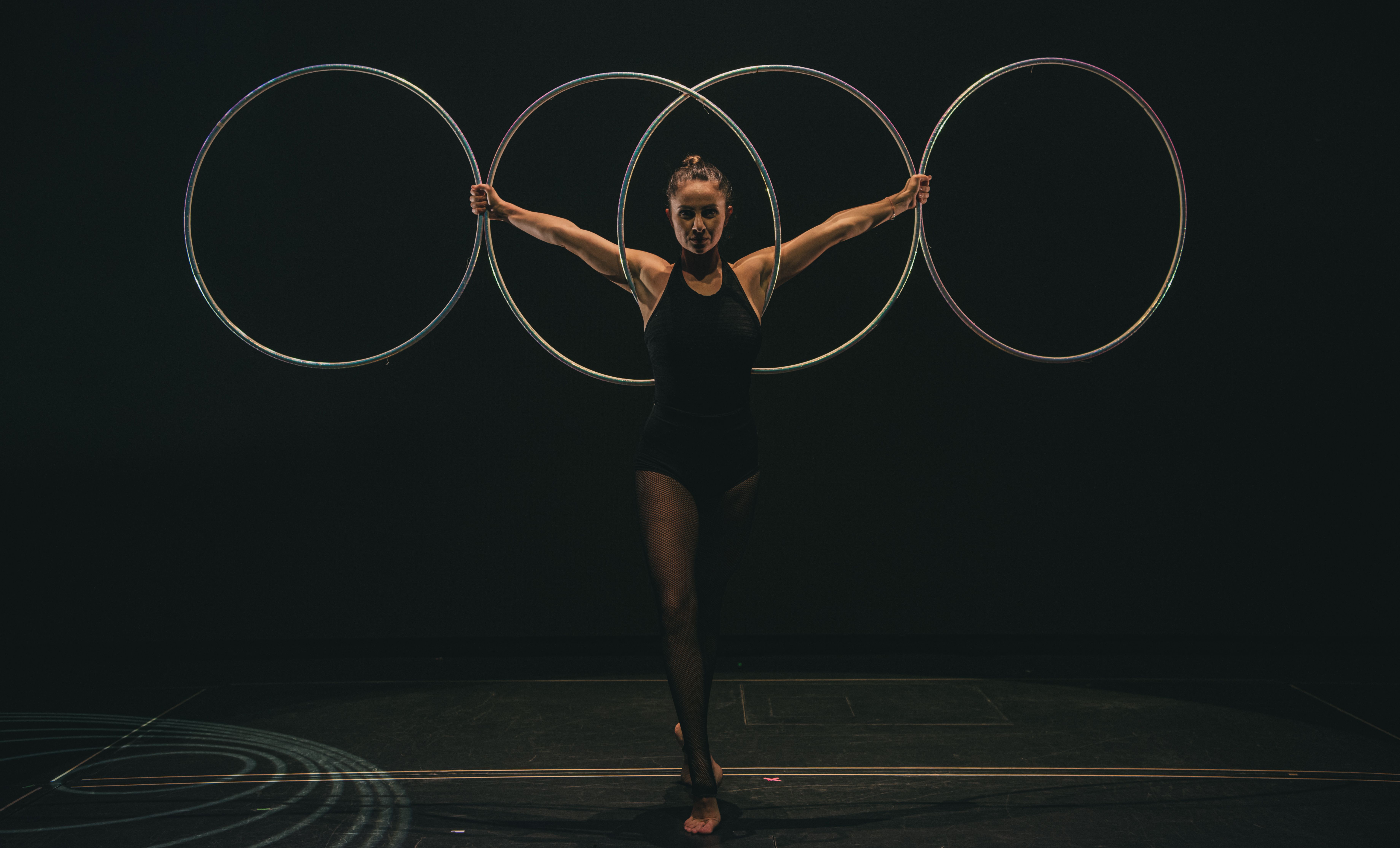 A skilled gymnast performs with hoops on stage, showcasing grace and control in a dramatic setting.