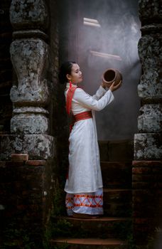 A woman in cultural attire holds a clay pot amidst ancient stone architecture.