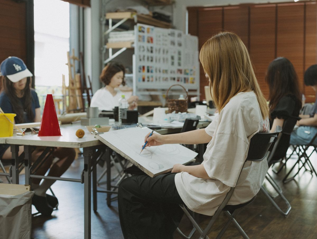 Group of students in Tokyo art class sketching at desks with art supplies