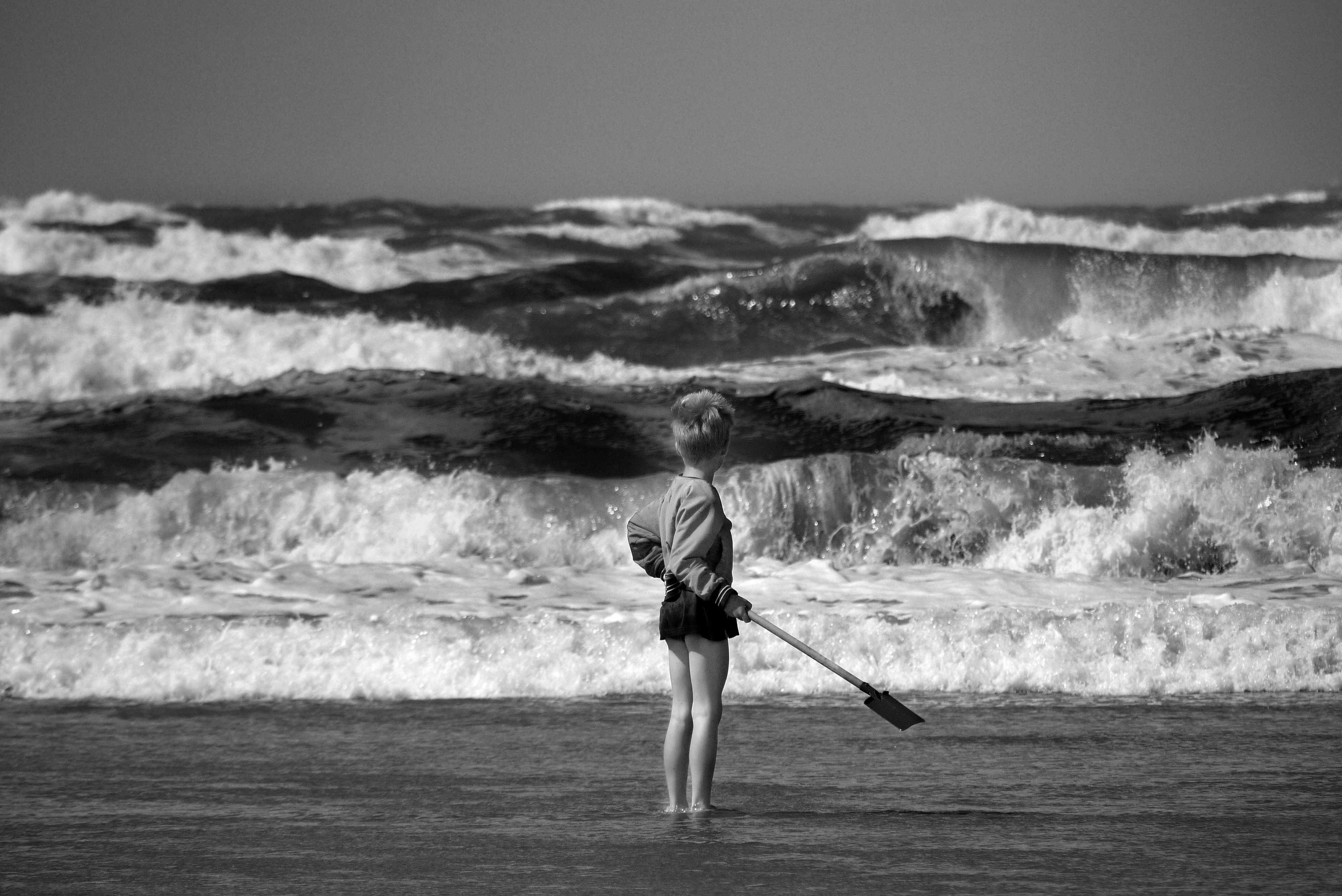 A child stands at the shore, gazing at the strong waves in Overveen, Netherlands.