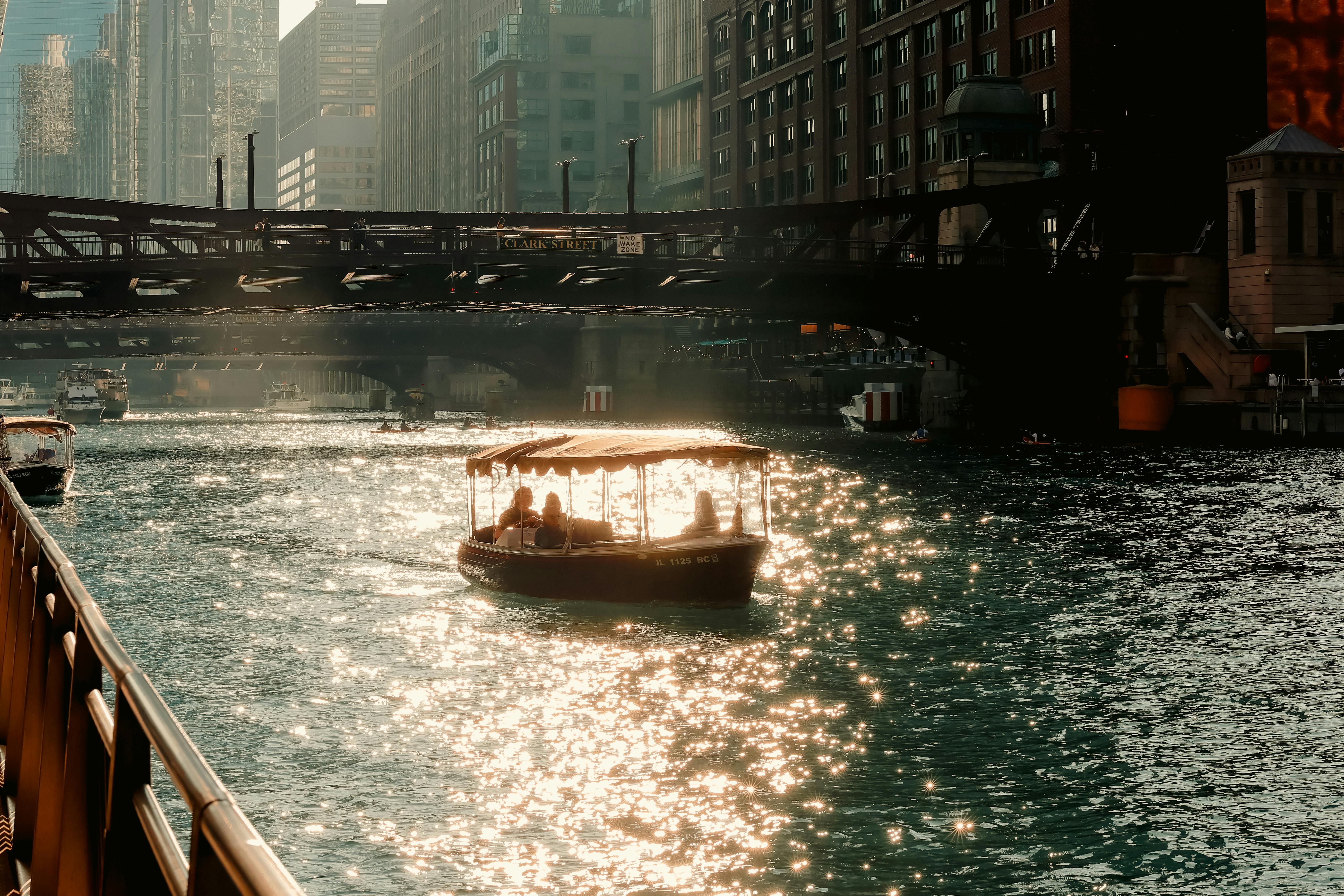 A picturesque view of a boat gliding on the reflective Chicago River under Clark Street Bridge during golden hour.