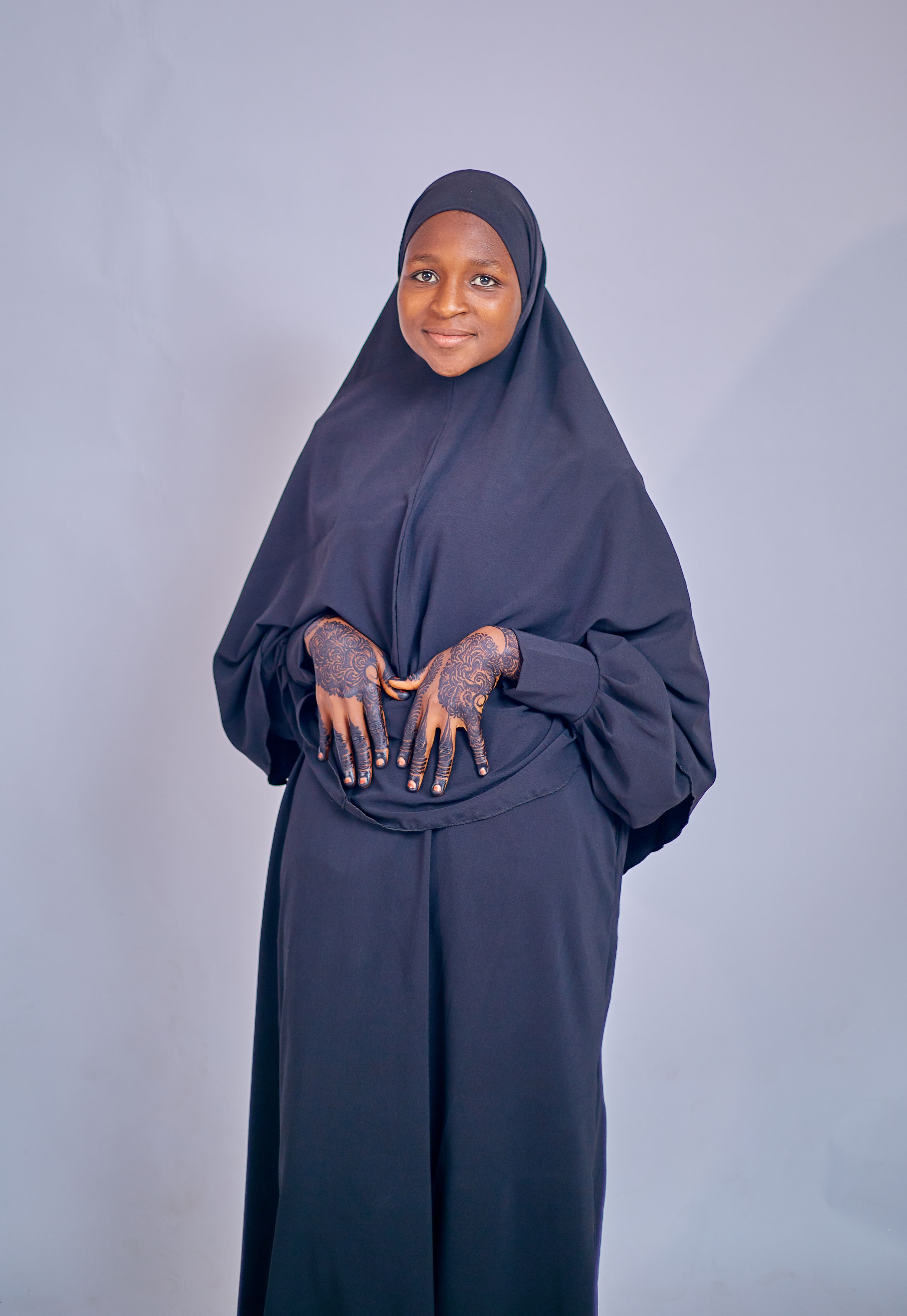 Portrait of a young woman wearing a hijab and showcasing intricate henna designs on her hands.