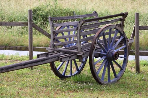 Free A rustic wooden cart stands amidst a lush green field on a sunny day. Stock Photo