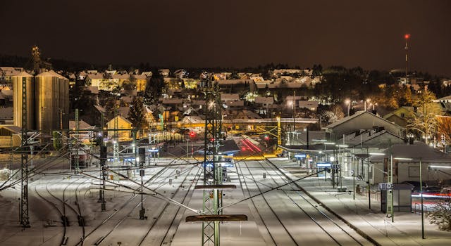 夜间，一座被雪覆盖的火车站亮起灯光，展现了城市的建筑与交通