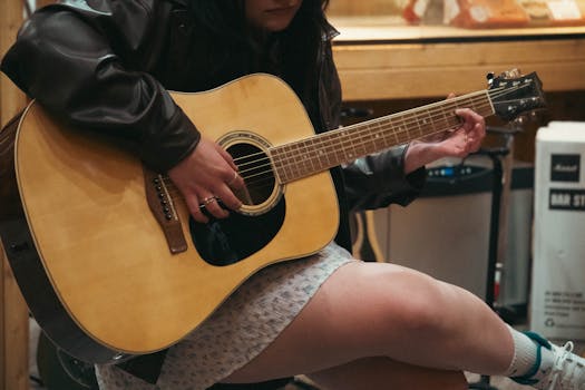 Close-up of a young woman playing an acoustic guitar indoors, capturing a moment of musical creativity.