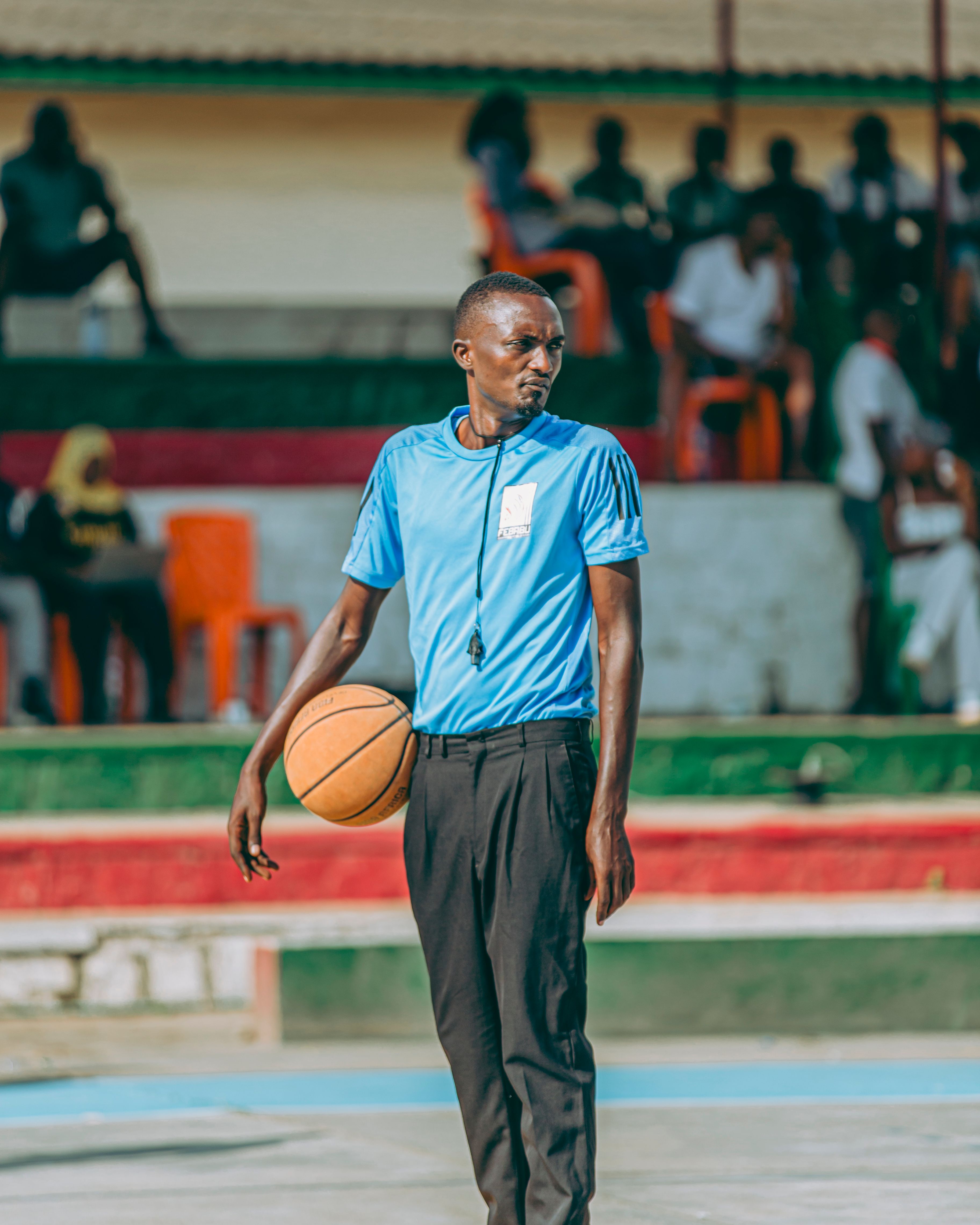 A basketball referee in blue uniform holds a basketball on an outdoor court.