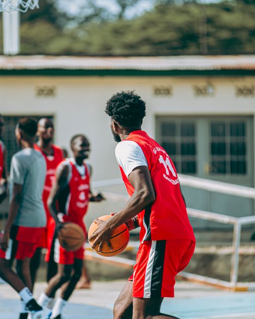 Free Young men in red uniforms playing basketball outside on a sunny day. Stock Photo