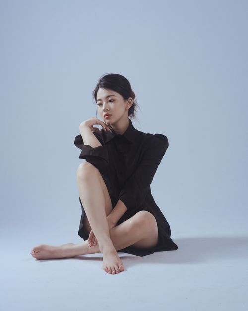 Free Thoughtful woman in black dress seated on the floor in a minimalist indoor setting. Stock Photo