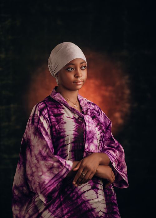 Free Elegant portrait of a woman in purple tie-dye attire and headscarf with a warm backdrop. Stock Photo