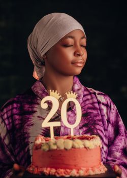 A joyful young woman celebrates her 20th birthday with a vibrant frosted cake.