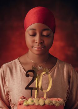 Portrait of a young woman in a red headscarf celebrating her 20th birthday with a cake.