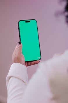 Smartphone with green screen held by person indoors, perfect for mockup or design use.
