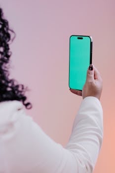 Adult holding smartphone with a green screen in modern indoor setting.