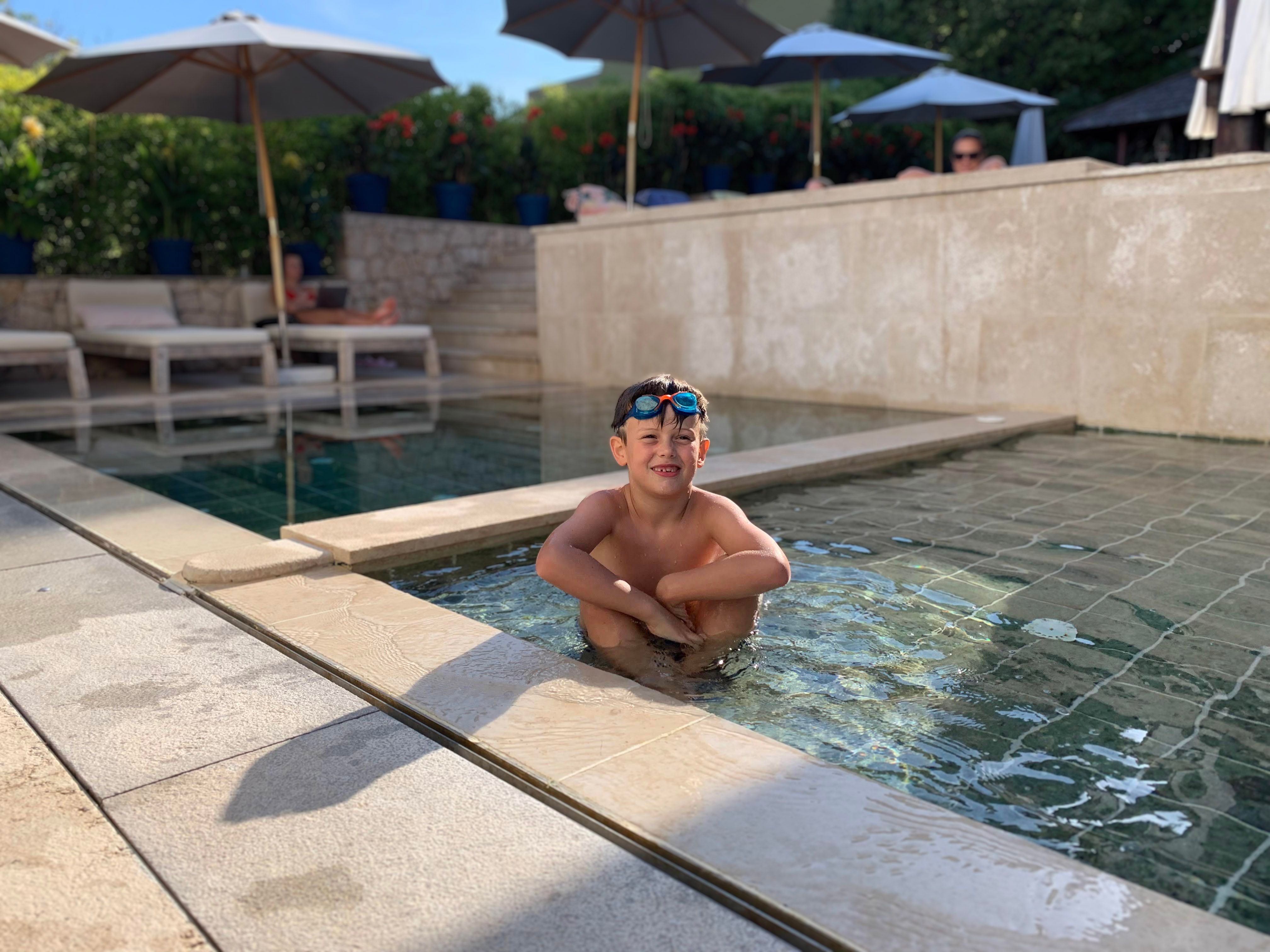 Criança feliz com óculos de natação em piscina ensolarada de hotel de luxo familiar.