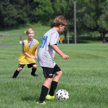 Two boys playing soccer outdoors in Doylestown, Pennsylvania, on a sunny day.