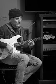 A man playing an electric guitar indoors, captured in a monochromatic style.