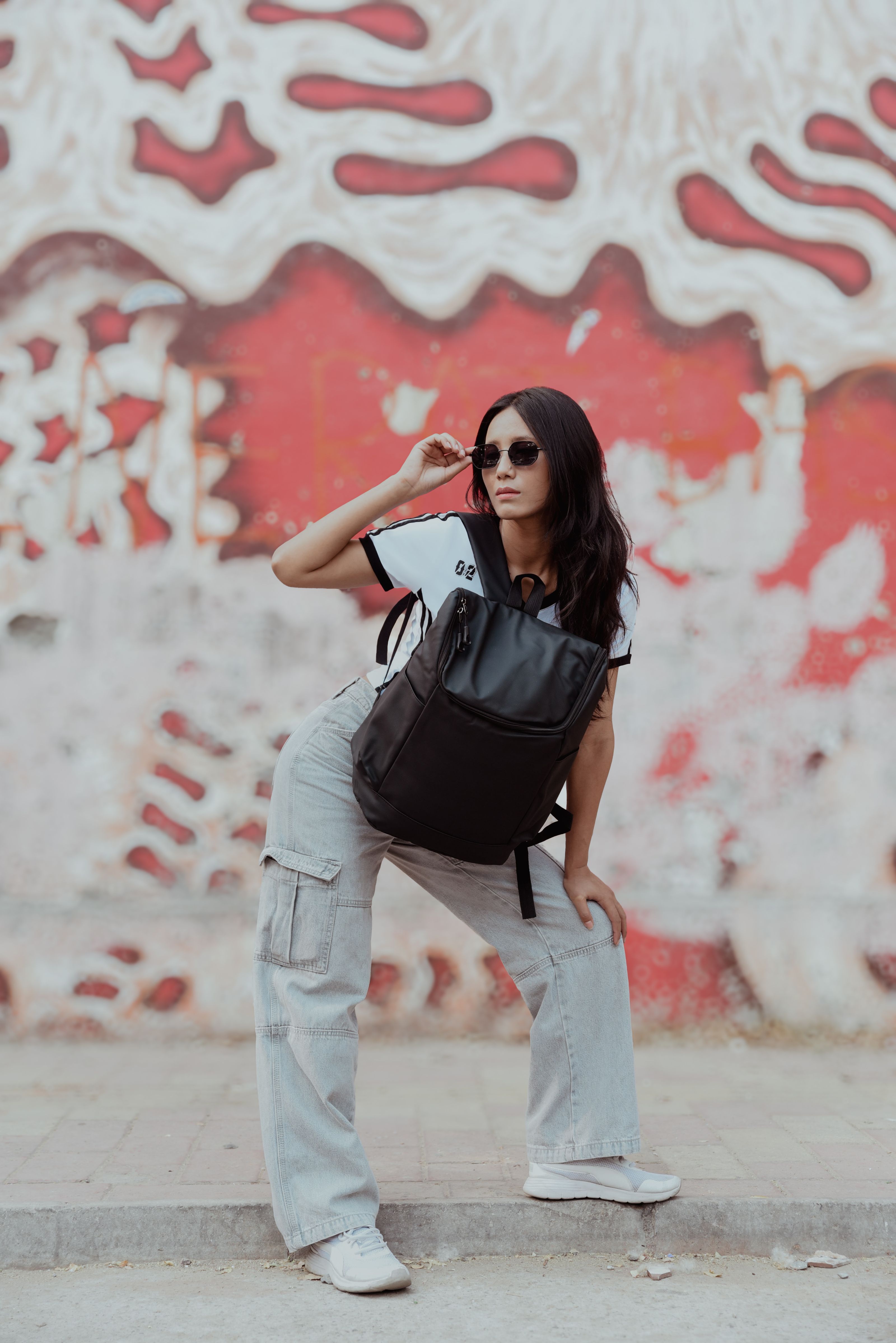 Mulher fashion em um traje casual posando com confiança contra uma parede de grafite colorida.