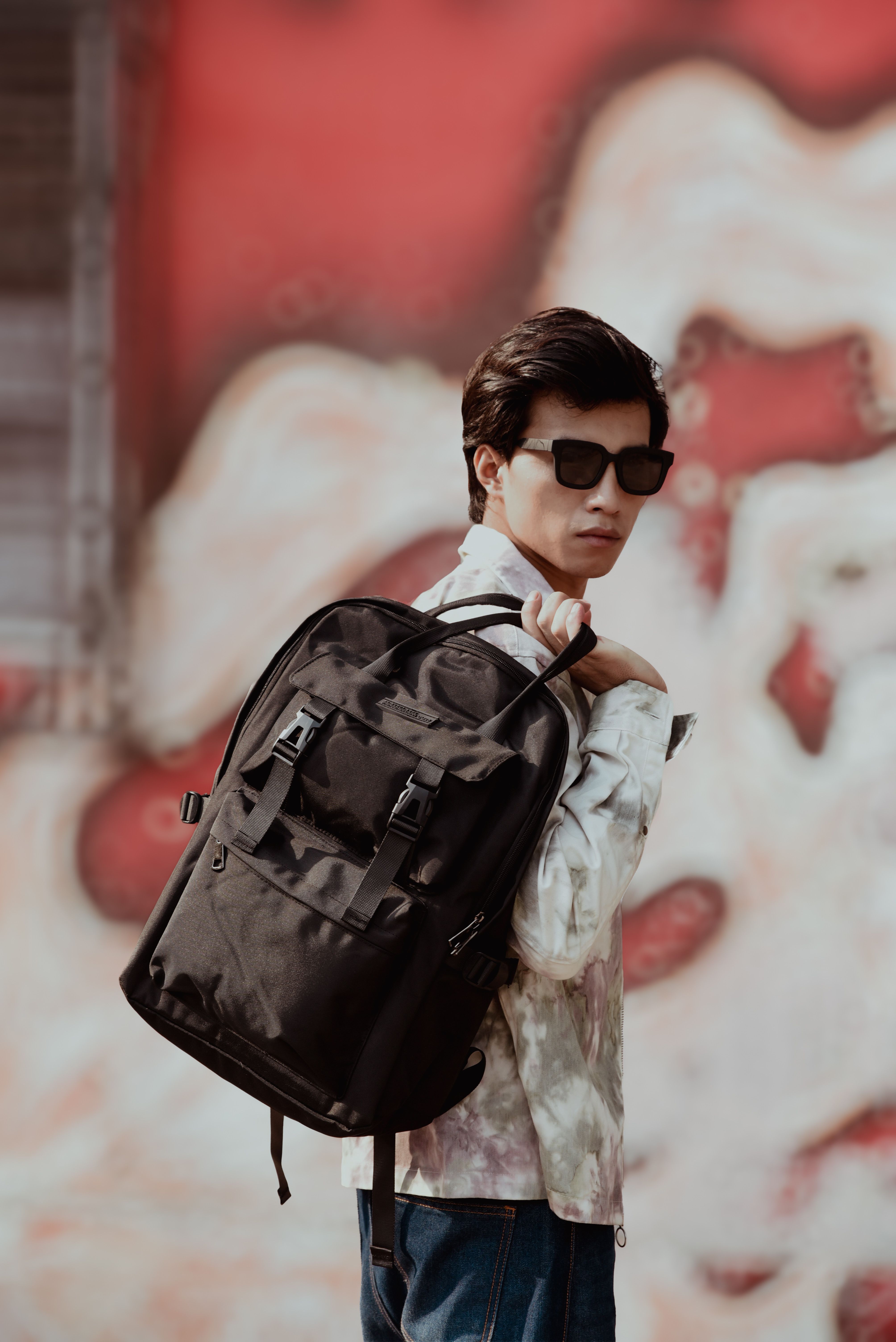 Stylish young man wearing sunglasses and backpack in front of graffiti wall.