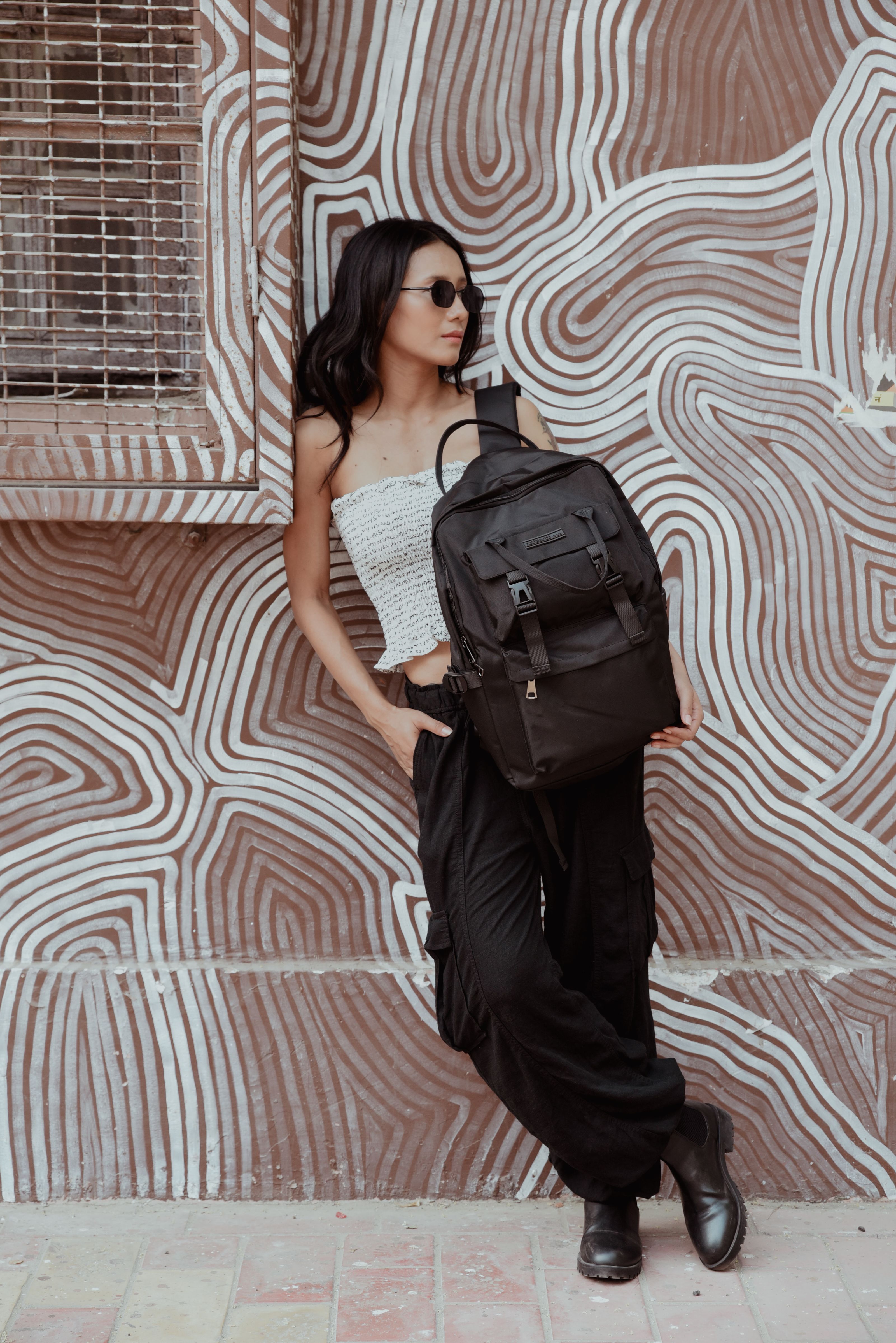 Mulher fashion posa com mochila contra fundo artístico, moda estilo urbano.