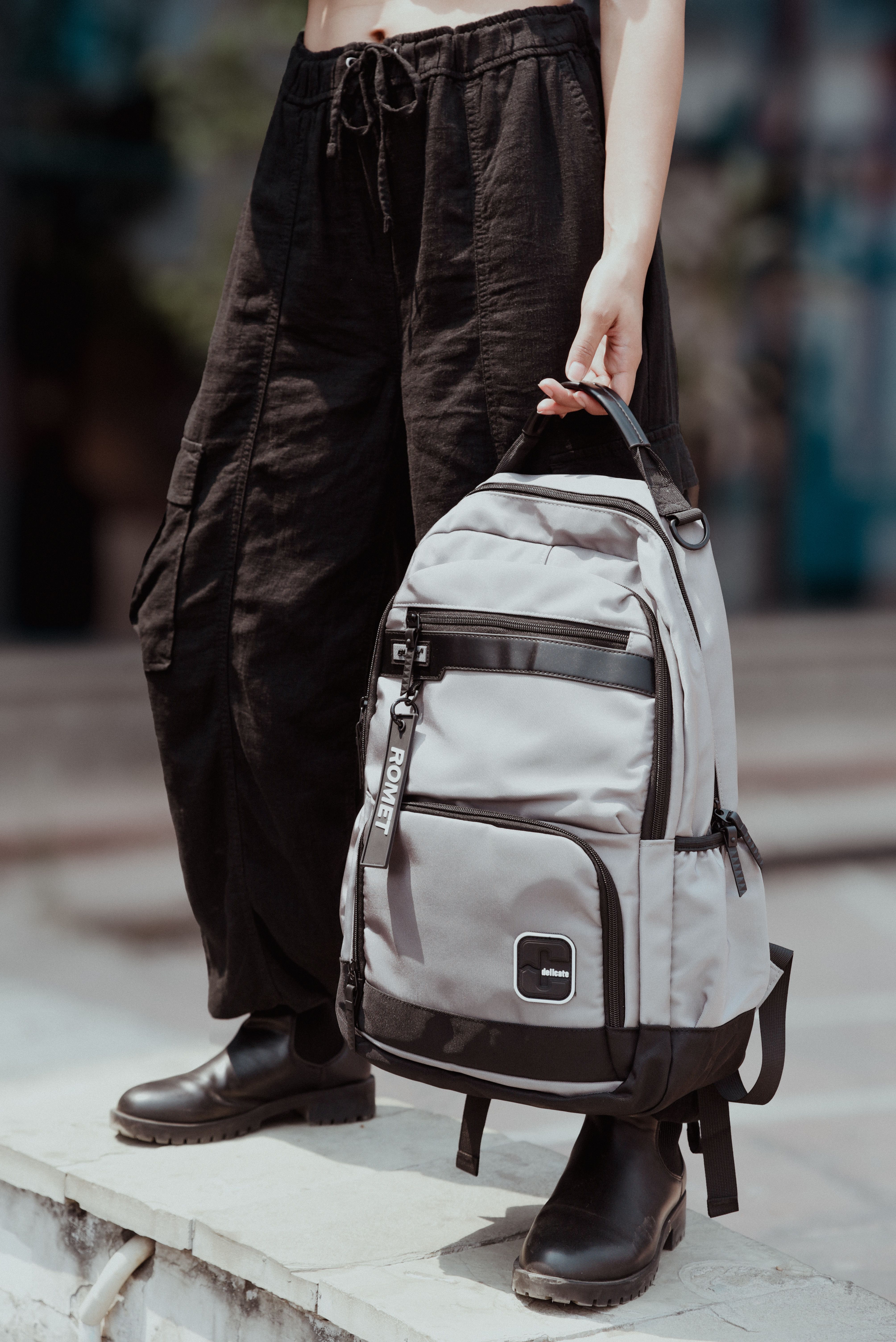 Person holding a stylish gray backpack outdoors, emphasizing casual fashion style.