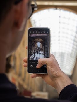 A man photographing a stylish gallery in Bordeaux with his phone.
