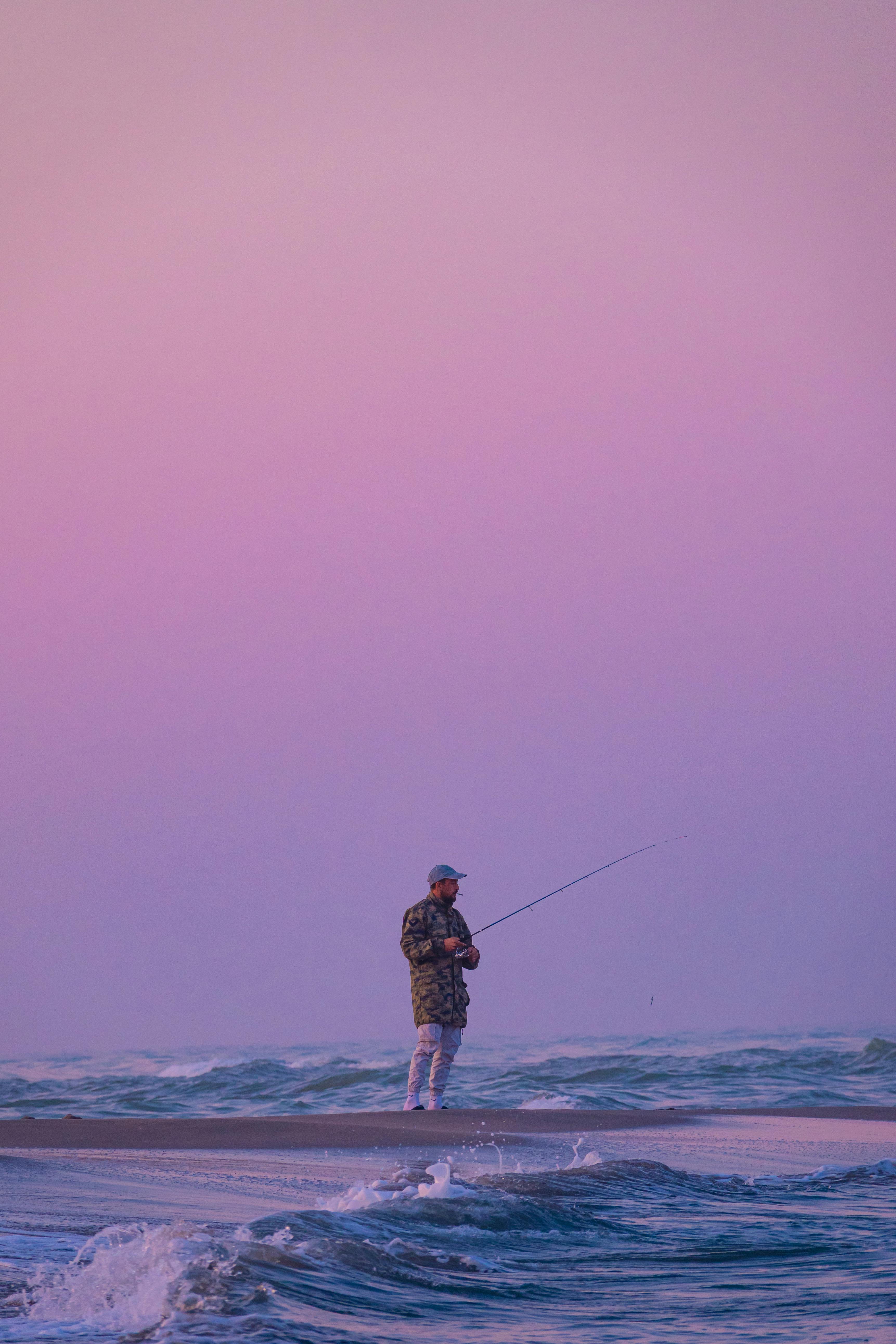 A fisherman casting his line against a stunning pink sunset in Muğla, Türkiye.