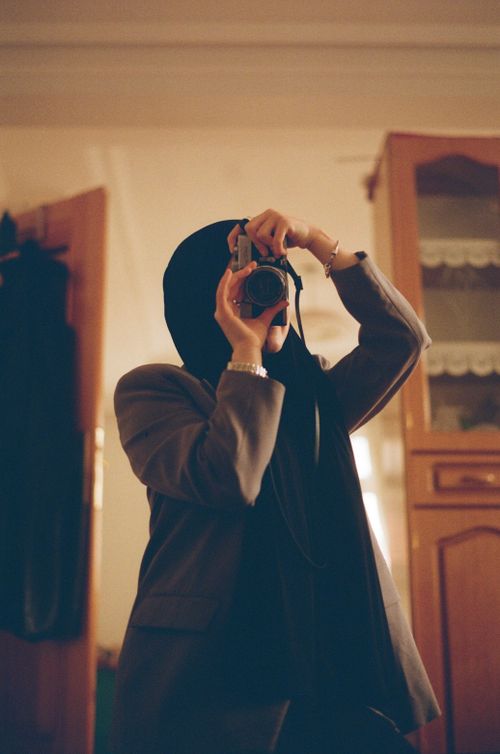 Free Woman in hijab taking a photo indoors with a vintage camera. Stock Photo