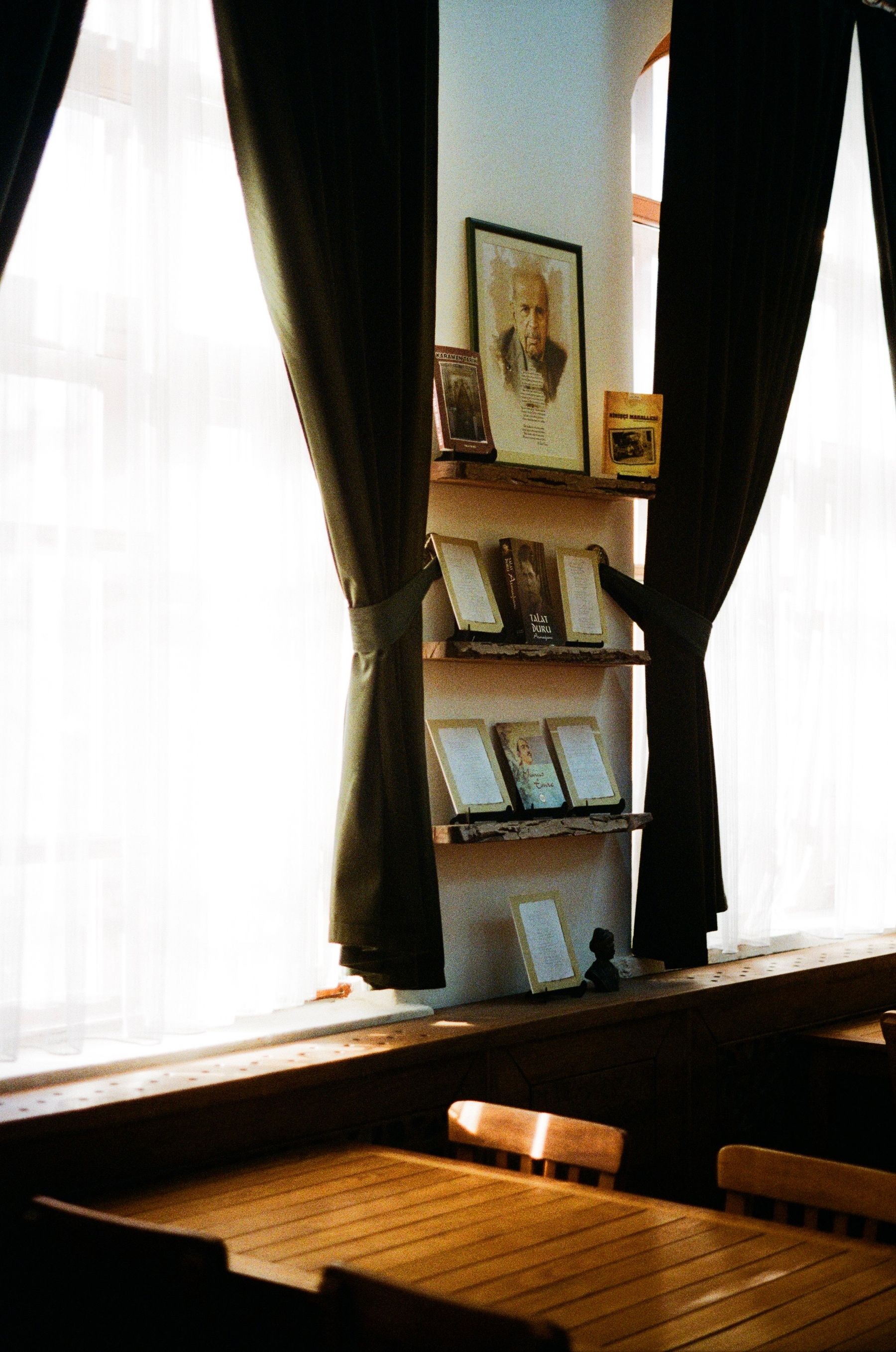 Warm study corner with wooden bookshelf, vintage photograph, window light and dark drapes