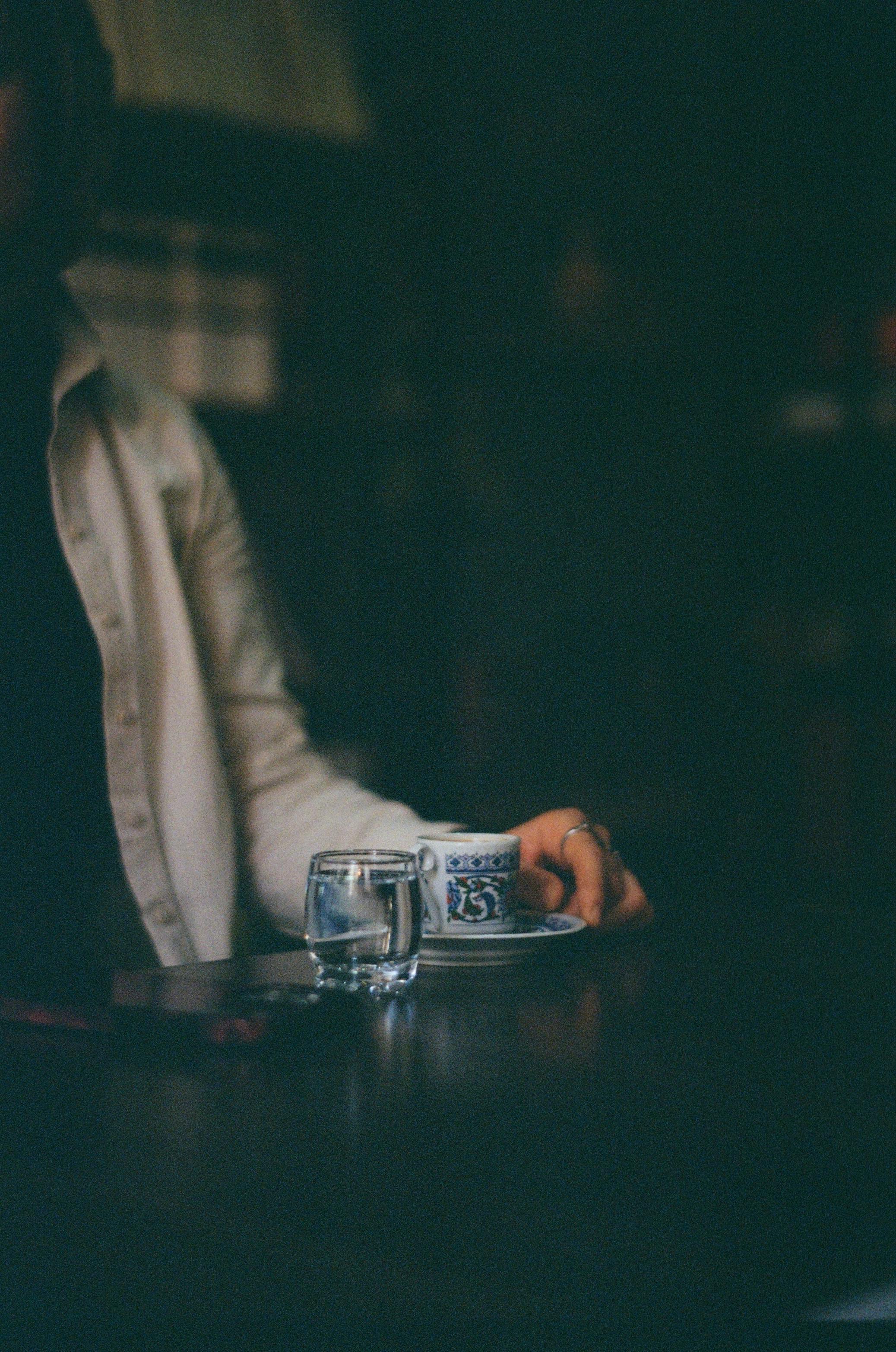 Gratuit O persoană savurează cafeaua într-o cafenea slab luminată, creând o atmosferă caldă și intimă. Fotografie de stoc