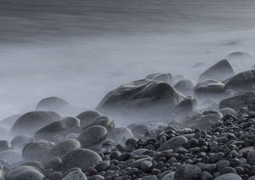 Free Tranquil scene of smooth stones and gentle waves on a misty coast, evoking peace and serenity. Stock Photo