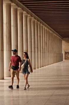 Couple walking through a classic Greek colonnade in Athens, Greece, exploring history and architecture.