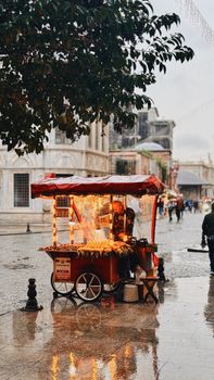 A vibrant street vendor stall amidst a rainy city backdrop with glowing lights.