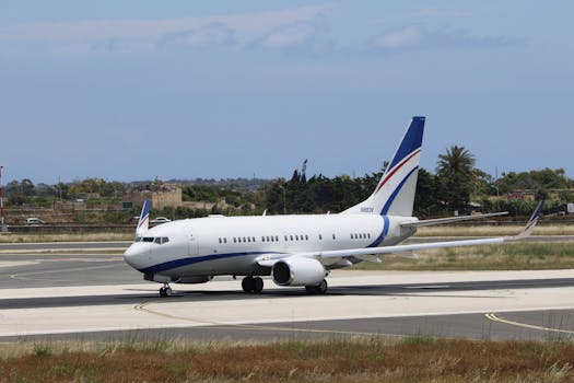 A white commercial jet with blue accents on an airport runway against a clear blue sky.