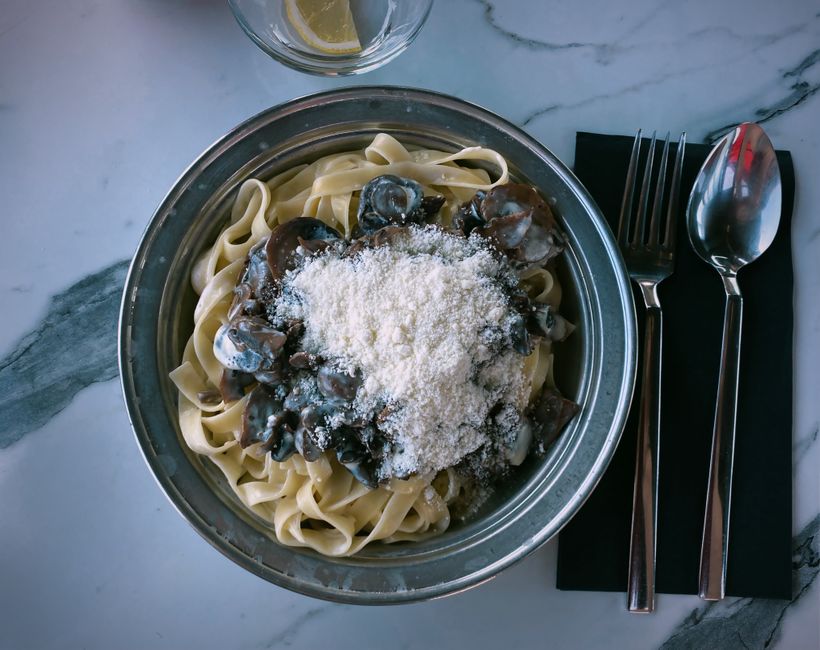 Close-up of tagliatelle pasta with mushrooms and Parmesan on marble.