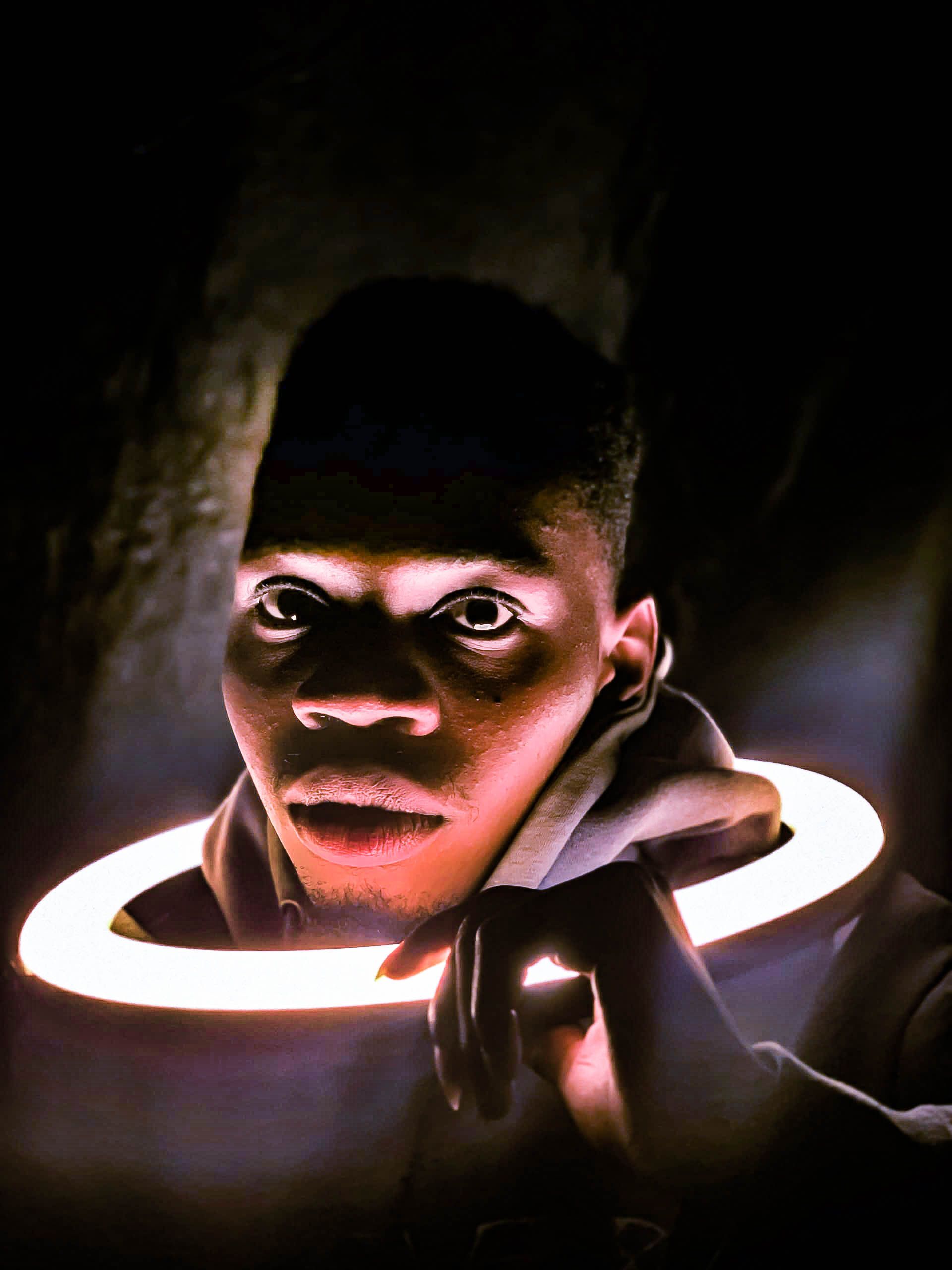 A striking portrait of an adult man illuminated by a circular light in a dark setting.