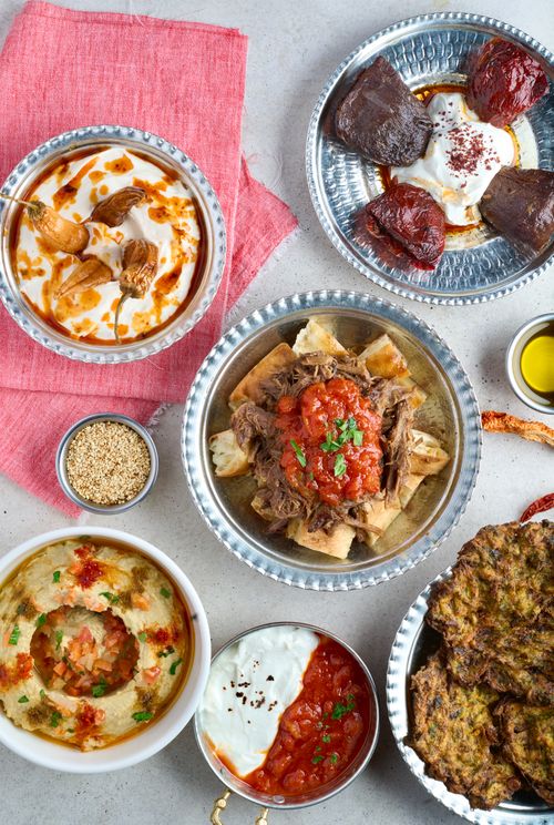 Free Delicious variety of Middle Eastern dishes featuring hummus, roasted meats, and sauces. Stock Photo