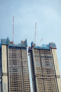 Two modern skyscrapers under construction with cranes on a clear day.