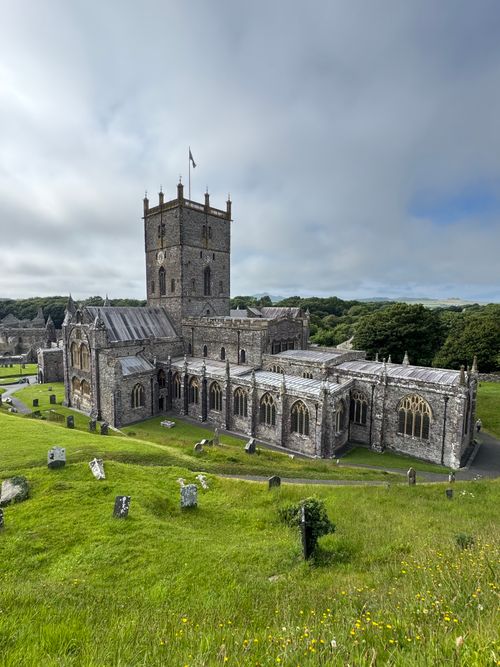 Free Beautiful view of St Davids Cathedral surrounded by green fields under a cloudy sky in Wales. Stock Photo