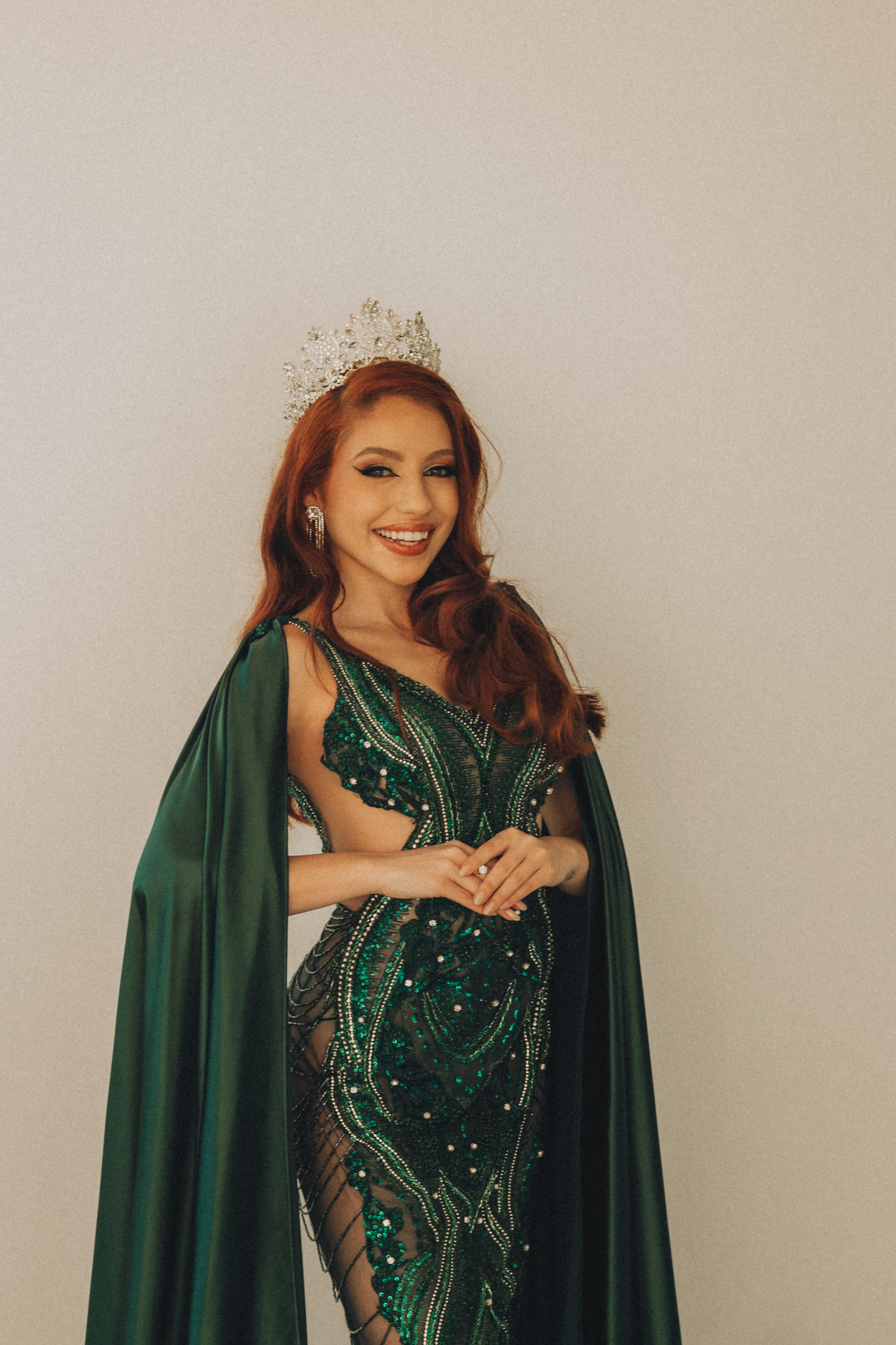 A woman in an ornate green gown and crown, exuding elegance indoors.