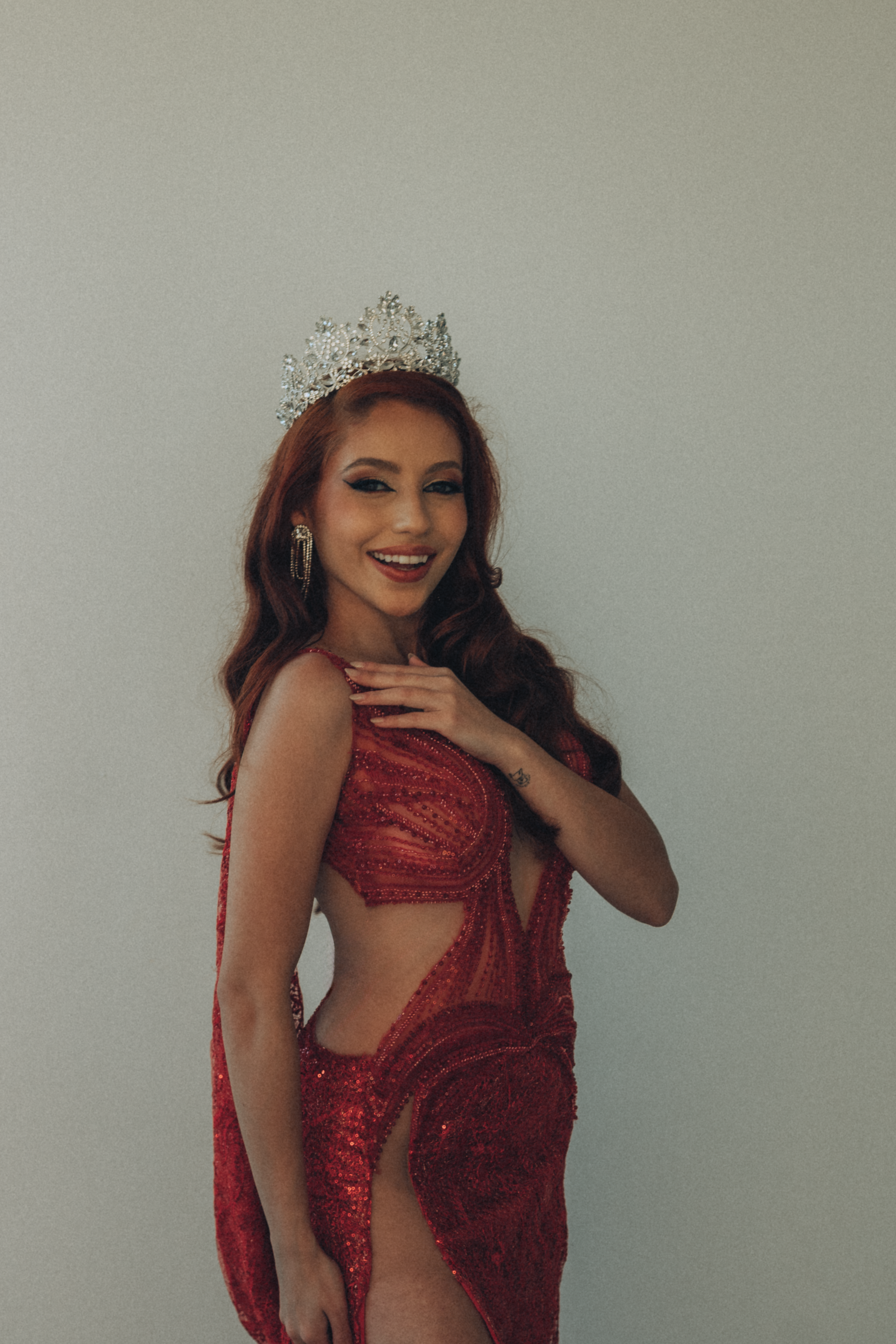 Smiling woman in a dazzling red sequin gown and crown, embodying elegance.