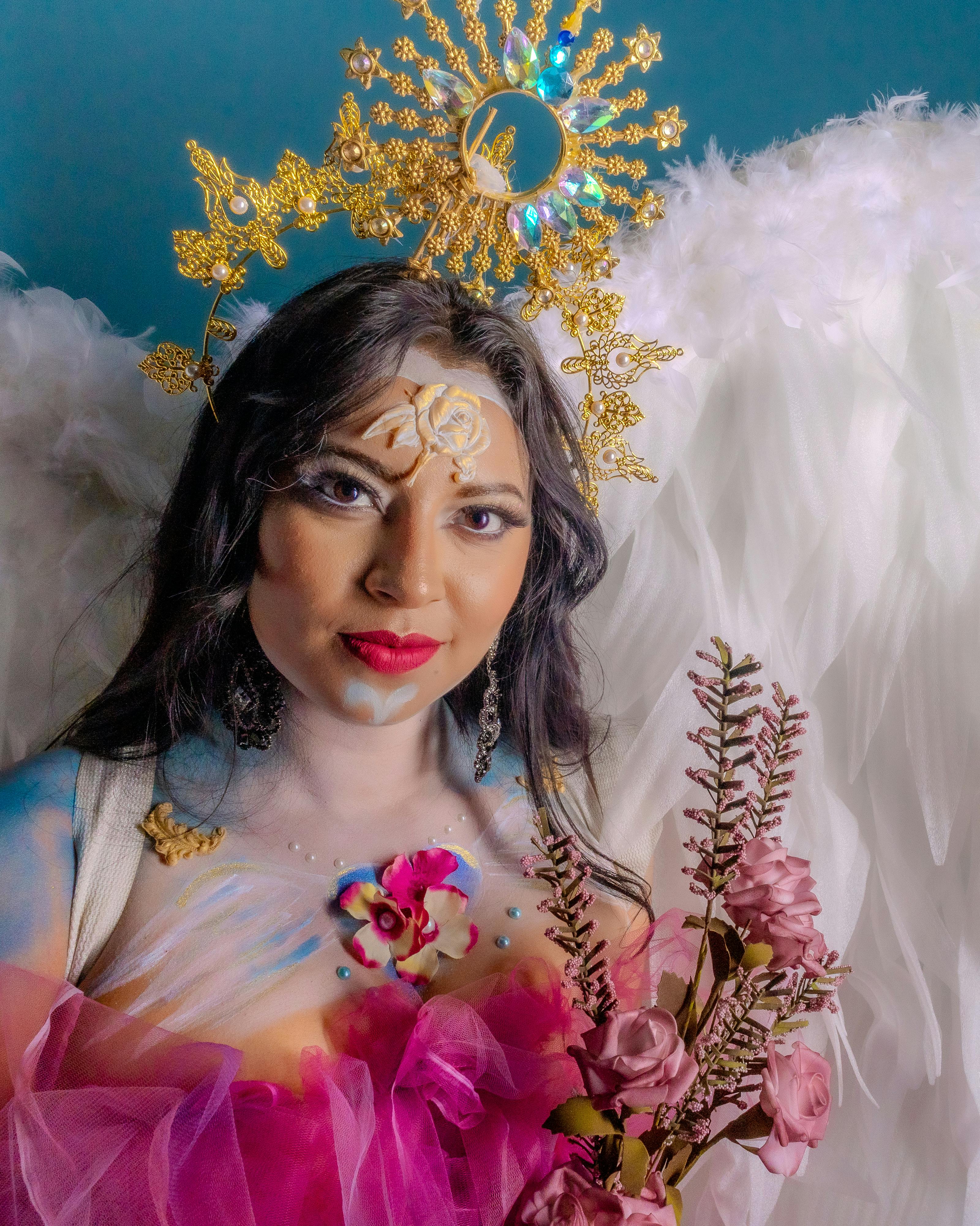 Vibrant artistic portrait of a woman with angelic wings, flowers, and creative makeup.