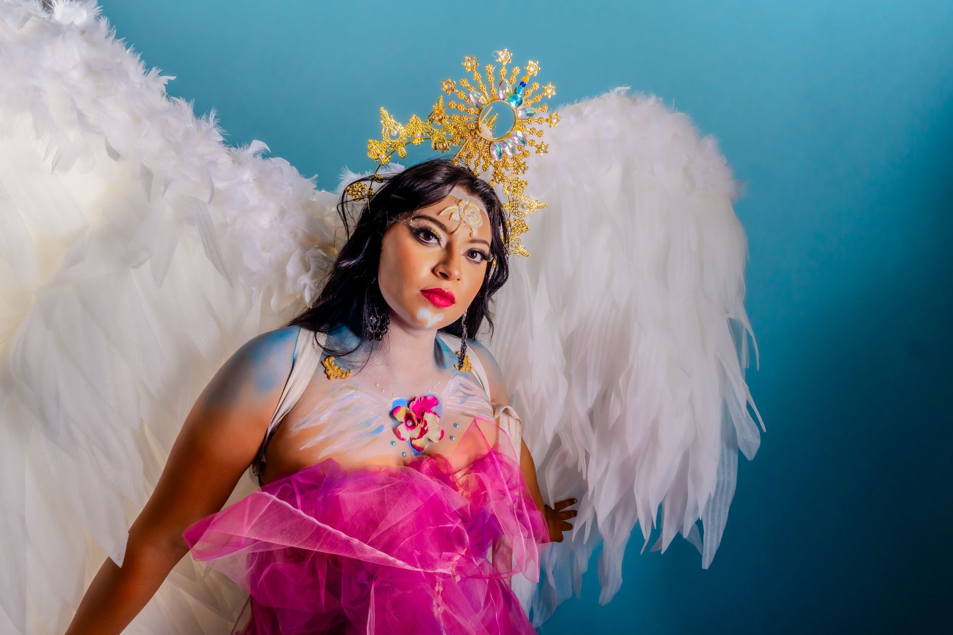Dramatic portrait of a woman with angel wings, adorned with artistic makeup and a whimsical crown.
