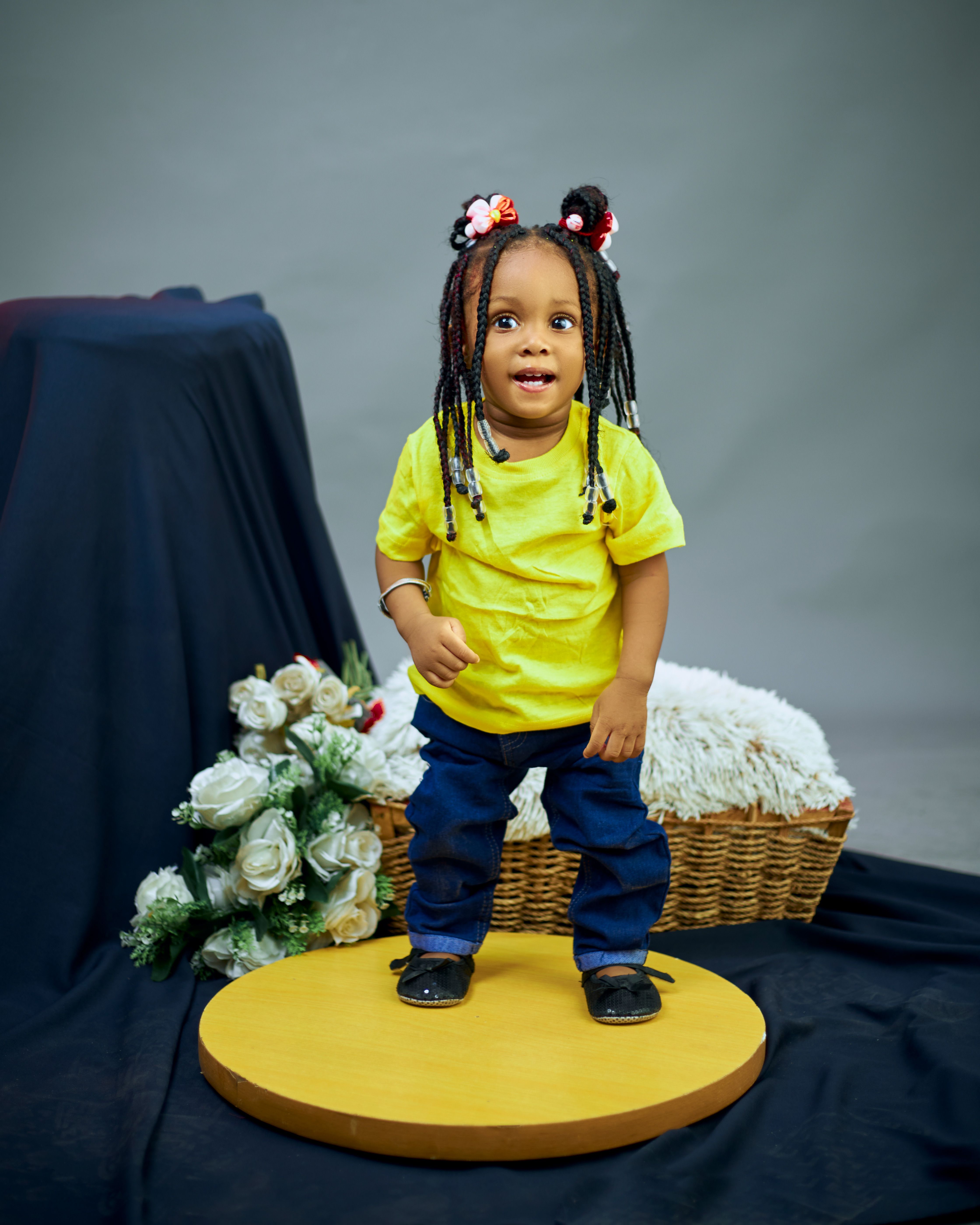 Cute child standing on podium in studio with flowers and basket.